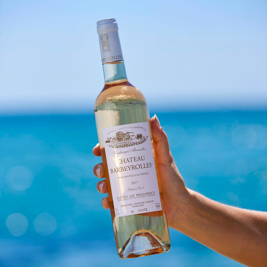 Bottle of Château Barbeyrolles Pétale de Rose Wine held aloft with Ocean in Background
