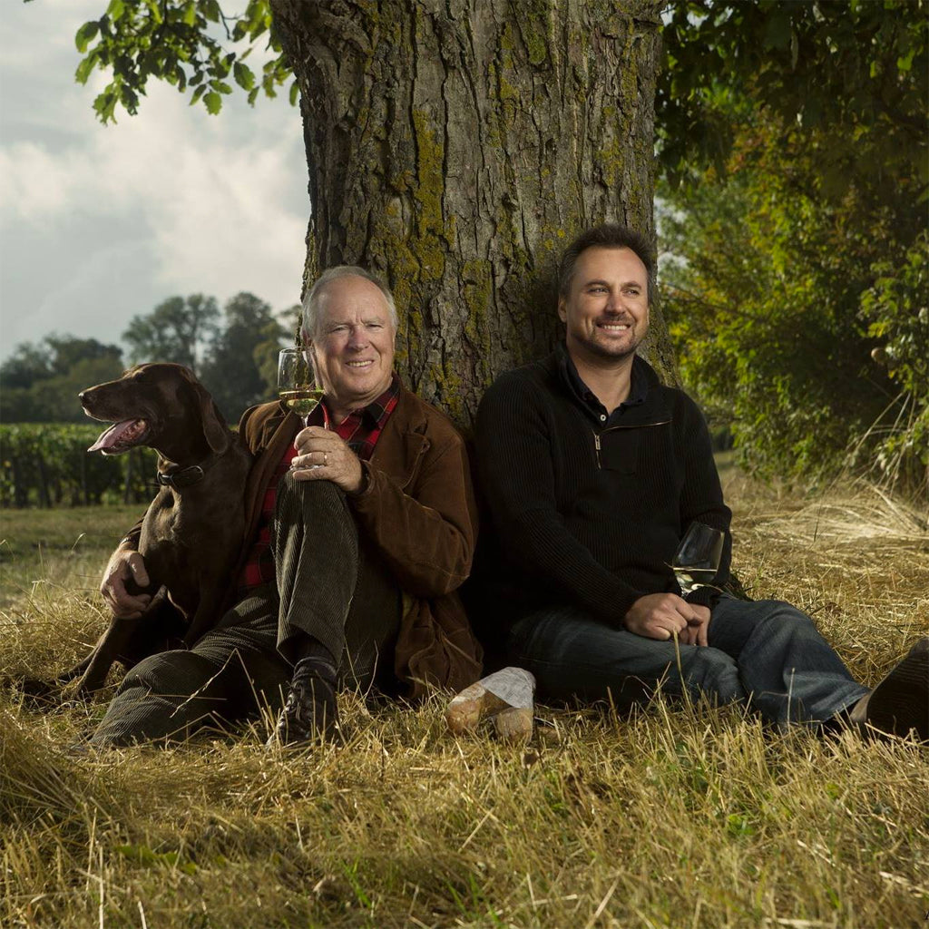 Jean-Marc and Julien Brocard sitting at the foot of a tree each with glass of wine in hands